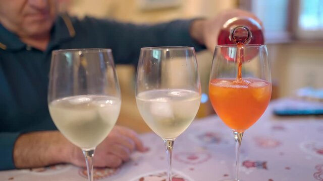 Close-up of bartender's hand holding alcohol bottle and pouring aperol in wineglasses with prosecco and ice cubes, man preparing refreshing summer fizzy cocktail drink for party or celebration event