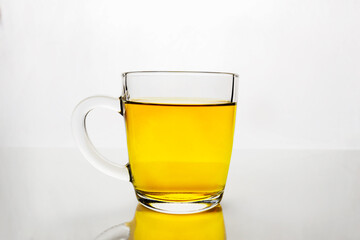 Transparent glass cup with yellow liquid on white surface. Mug of tea or juice.