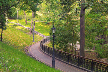 Park Saint Volodymyr Hill in early autumn. Nature landscape. Narrow winding cobble stone alleys with vintage lanterns. Fallen leaves in green grass. Autumn morning in Kyiv, Ukraine