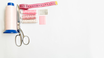 items for sewing: scissors, three pink small thread and one large spool for the sewing machinechalk, needles, centimeter on the white backround with copy space