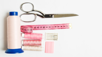 items for sewing: scissors, three pink small thread and one large spool for the sewing machinechalk, needles, centimeter on the white backround with copy space