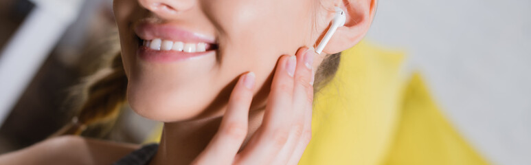 Fototapeta premium Panoramic shot of young woman touching wireless earphone