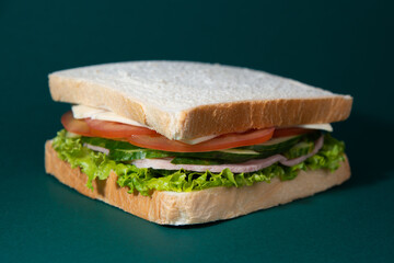 Sandwich with ham and salad on dark green background
