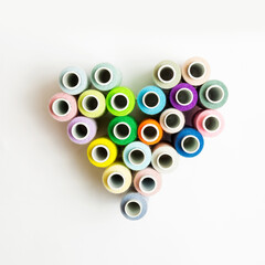 heart made of spools of sewing multicolored thread on a white background.Top view