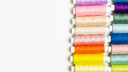 many multi-colored small spools with sewing thread on the right lined up in a line on a white background with copy space on the left
