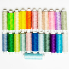 many multi-colored small spools with sewing thread in line on a white background
