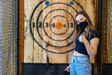 Teen girl stands next to axe stuck in an axe throwing target