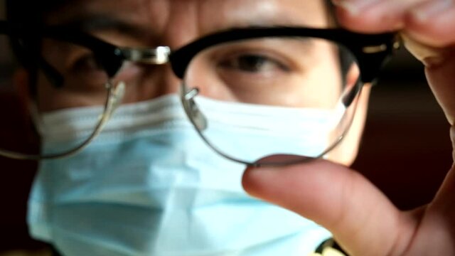 An Asian man examining and wearing eyeglasses