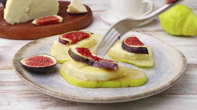 Summer appetizer with pear, cottage cheese, figs and honey cut with a fork on a white wooden background. Side view, close up.