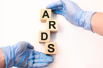 Word ARDS on wooden cubes held by hands in protective gloves on a white background with available space for copying. the medicine