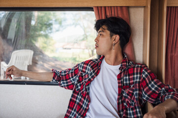 Young asian man in scott shirt relaxing with smoking cigarette in campervan