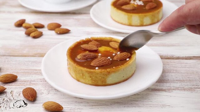 Sweet tartlets with caramel decorated with almonds cut with a spoon on white wooden background. Side view, close up.