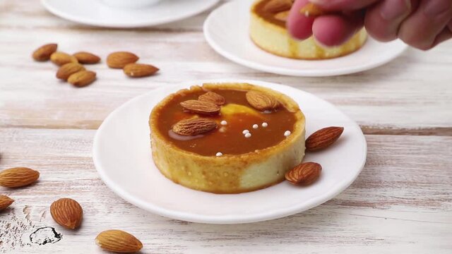 Sweet tartlets with caramel decorated with almonds on white wooden background. Side view, close up.