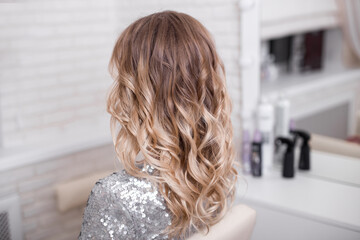 Female back with long, curly, ombre, blonde hair, in hairdressing salon
