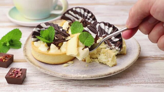 Sweet tartlets with chocolate and cheese cream cut with a spoon on white wooden background. Side view, close up.