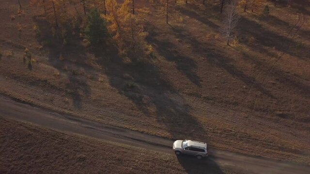 Aerial 4k shot. A 4x4 car rides through a colorful mountain forest at sunset, leaving a cloud of dust behind it. World tour concept. Drone shooting, zooming, and following focus.
