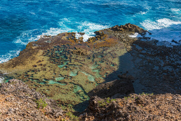 Caye partiellement recouverte d'eau au pied d'une falaise tropicale érodée avec des couleurs magnifique et le ressac de l'océan venant frapper la côte de Guadeloupe