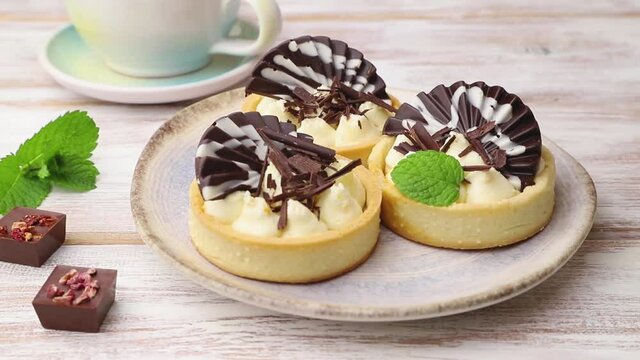 Sweet tartlets with chocolate and cheese cream decorating with mint on white wooden background. Side view, close up.