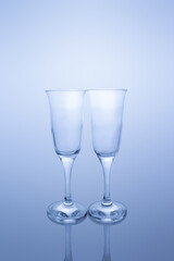Two empty transparent glass goblets on reflective surface in blue tint