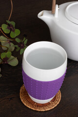 Tea cup with hot water on a wooden table surface and 4-leaves clovers on the background, top view
