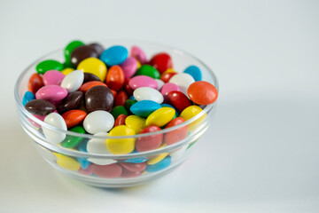 Colored candy dragees in a bowl, and poured on a white background.