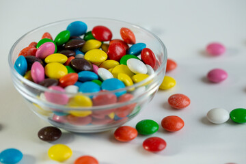Colored candy dragees in a bowl, and poured on a white background.