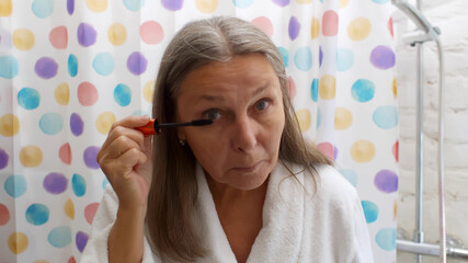 Portrait of senior woman putting mascara standing in bathroom in morning