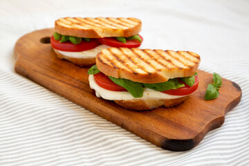 Tasty Grilled Caprese Panini (Mozzarella, Tomatoes and Basil) on a rustic wooden board, side view.