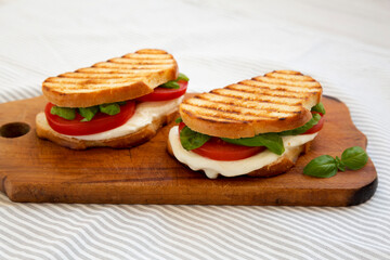 Tasty Grilled Caprese Panini (Mozzarella, Tomatoes and Basil) on a rustic wooden board, side view. Close-up.