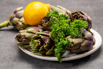 Fresh french petit violet artichokes heads cultivted in Brittany, France with lemon and parsley