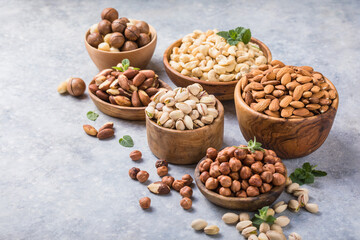 Assortment of nuts in a wooden bowls, on a gray background. Hazelnuts, pistachios, almonds, brazil nut, cashews