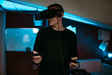 A man at home wearing virtual reality glasses. Holds controllers in his hands. Guy plays vr games. Neon lights © MoreThanProd