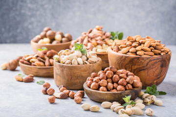 Assortment of nuts in a wooden bowls, on a gray background. Hazelnuts, pistachios, almonds, brazil nut, cashews