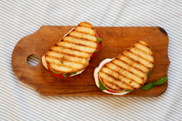 Tasty Grilled Caprese Panini (Mozzarella, Tomatoes and Basil) on a rustic wooden board, top view. Flat lay, overhead, from above.