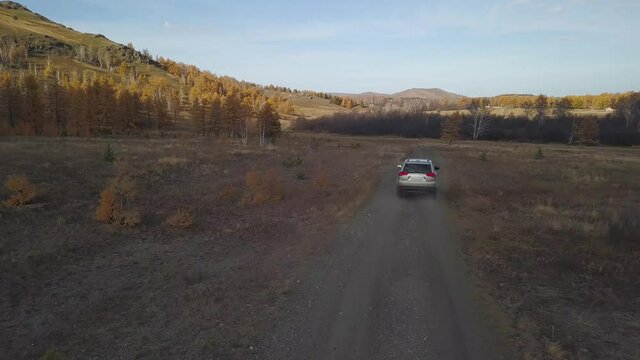 Helicopter shot 4к, tracking a car. Jeep with four-wheel drive 4WD travels on a rough forest road. Crossover tire tracks on the orange desert sand among a long range of amazing view mountains.