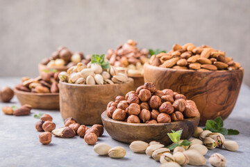 Assortment of nuts in a wooden bowls, on a gray background. Hazelnuts, pistachios, almonds, brazil nut, cashews