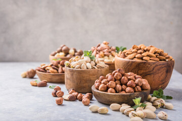 Fototapeta na wymiar Assortment of nuts in a wooden bowls, on a gray background. Hazelnuts, pistachios, almonds, brazil nut, cashews