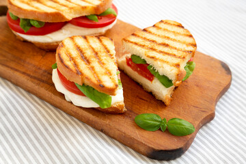 Tasty Grilled Caprese Panini (Mozzarella, Tomatoes and Basil) on a rustic wooden board, low angle view.