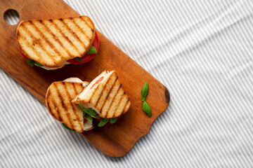 Tasty Grilled Caprese Panini (Mozzarella, Tomatoes and Basil) on a rustic wooden board, top view. Flat lay, overhead, from above. Copy space.