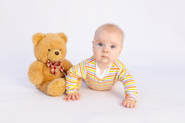 smiling baby girl 6 months old lies on a white isolated background in a bright bodysuit with a soft Teddy bear, space for text