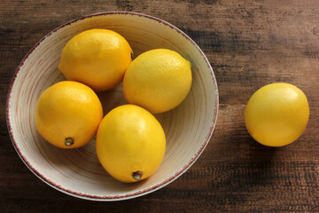 Ripe yellow lemons in a bowl on wooden table. Fresh citrus fruits on wood background. Flat lay, copy space. Rustic style composition.