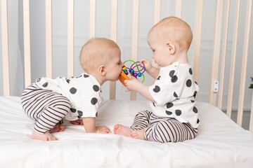 two twin babies 8 months old play in the crib, early development of children up to a year, the concept of the relationship of children of brother and sister, the child takes the toy from the other