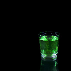 Green liquor in a shot glass with reflection against the black background