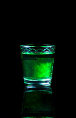 Green liquor in a shot glass with reflection against the black background