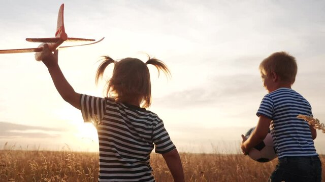 happy kids childs run with an airplane in the park. kid silhouette play plane. happy family dream freedom airplane concept. kids run on wheat field at sunset holds in his hands dream fun toy aircraft