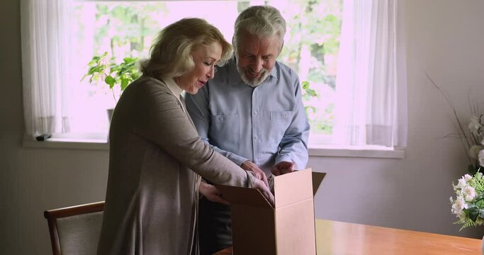 Middle-aged couple made order on internet online shop received items package open parcel feels satisfied by qualified goods from internet, got present form friends. Quick safe delivery service concept
