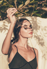 A girl of model appearance on a white background holds a tree branch in her hands that makes a shadow on her face