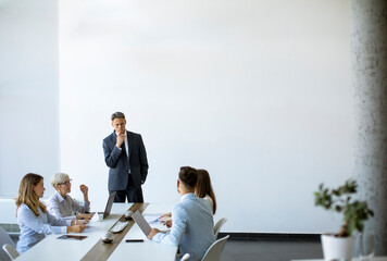 Group of business people with young adults and senior woman colleague on meeting at modern bright...