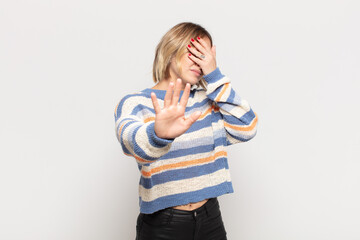 young pretty woman covering face with hand and putting other hand up front to stop camera, refusing...