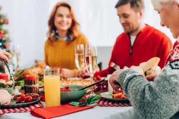 Selective focus of smiling grandma eating, sitting at festive table with family